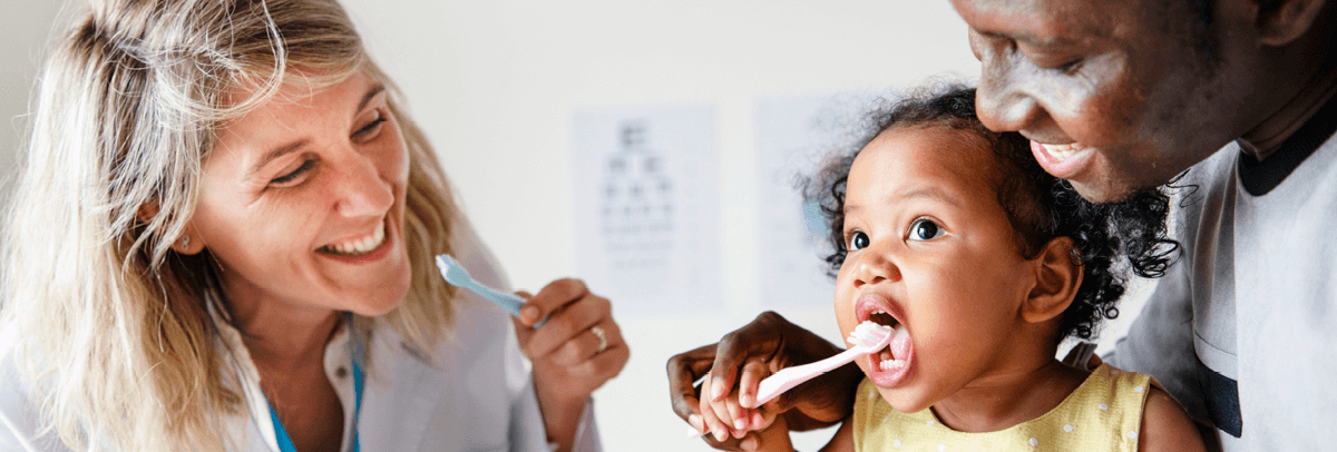 dentist with father and baby daughter female dentist showing father and baby daughter how to use toothbrush